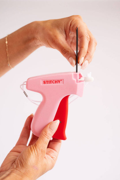 Hand using Tucky Stitchy pink tag gun with black cord, demonstrating needle mechanism