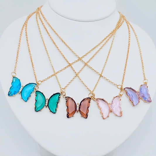 Five Mio Queena - Multicolor Glass Butterfly Pendant Necklaces from Mio Queena, featuring delicate glass pendants in blue, green, brown, pink, and purple on gold chains, are displayed on a white bust. Each hypoallergenic necklace is ideal for those with sensitive skin.