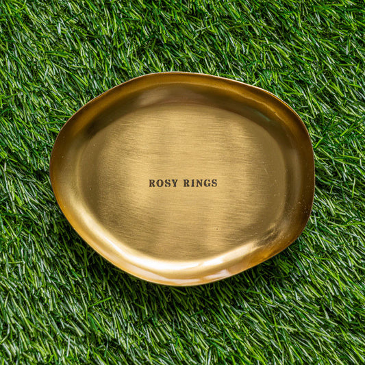 Rosy Rings Petite Botanical Candle Plate in brushed brass with embossed brand name on green grass background