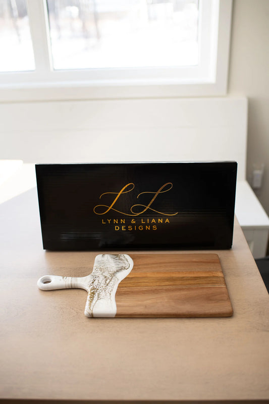Lynn & Liana Medium Acacia Cheese Board with white resin handle displayed with black branded packaging box