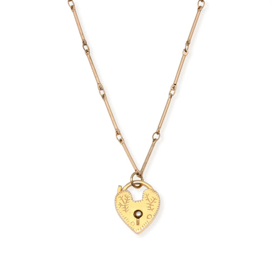 The Leslie Curtis Genesis Necklace by Leslie Curtis is a gold chain necklace with a heart locket pendant, featuring engraved details and a small keyhole at the center, complete with an extender for adjustable length.