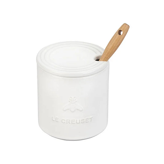White Le Creuset ceramic honey pot with wooden dipper, embossed logo visible on front