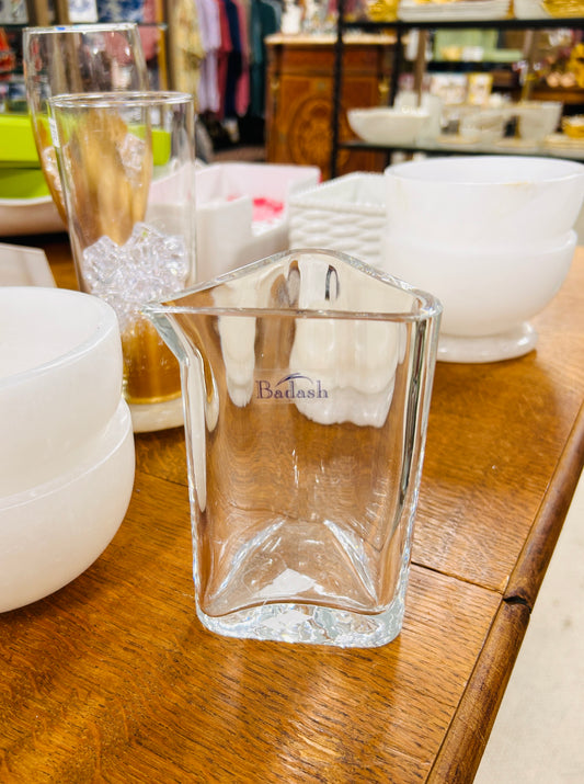 A Badash Triangle Individual Serving Pitcher, clearly labeled with the brand name "Badash," sits on a wooden table among white bowls and various glassware in a store.