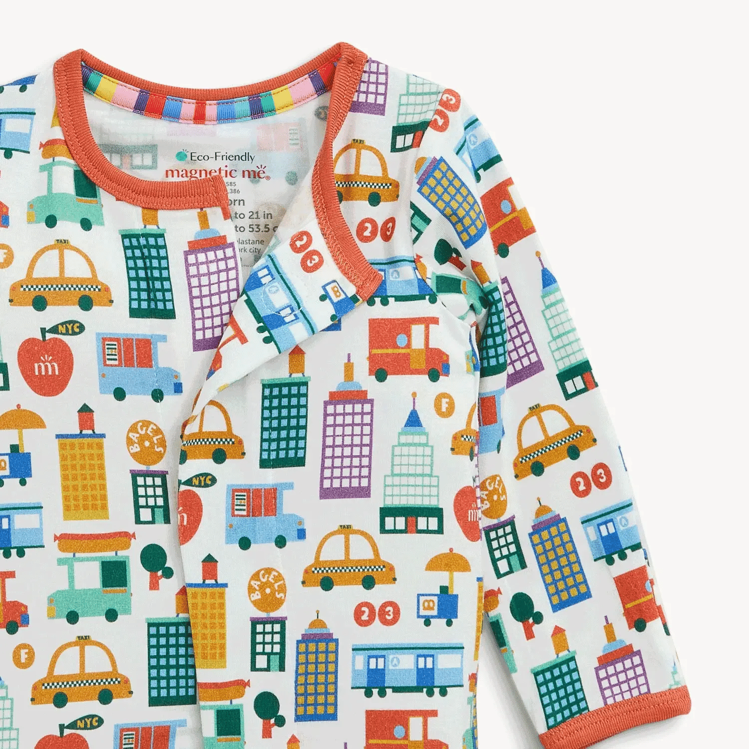 Magnetic Me "Know Your NYCs" Footie by Magnetic Me is a white modal sleeper featuring colorful city-themed prints of buildings, taxis, trees, and buses. It has soft fabric with orange trim and a magnetic closure near the neckline for easy dressing.