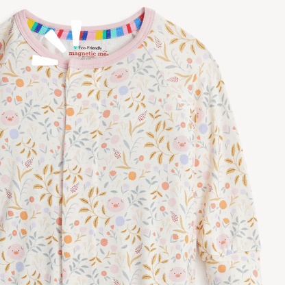 The Magnetic Me "Oinklet" Convertible Coverall from Magnetic Me features a charming floral and piglet pattern, light pink trim, and a colorful striped neckline. Made from sustainable modal fabric, it includes an eco-friendly tag that reads "Eco-Friendly magnetic me.