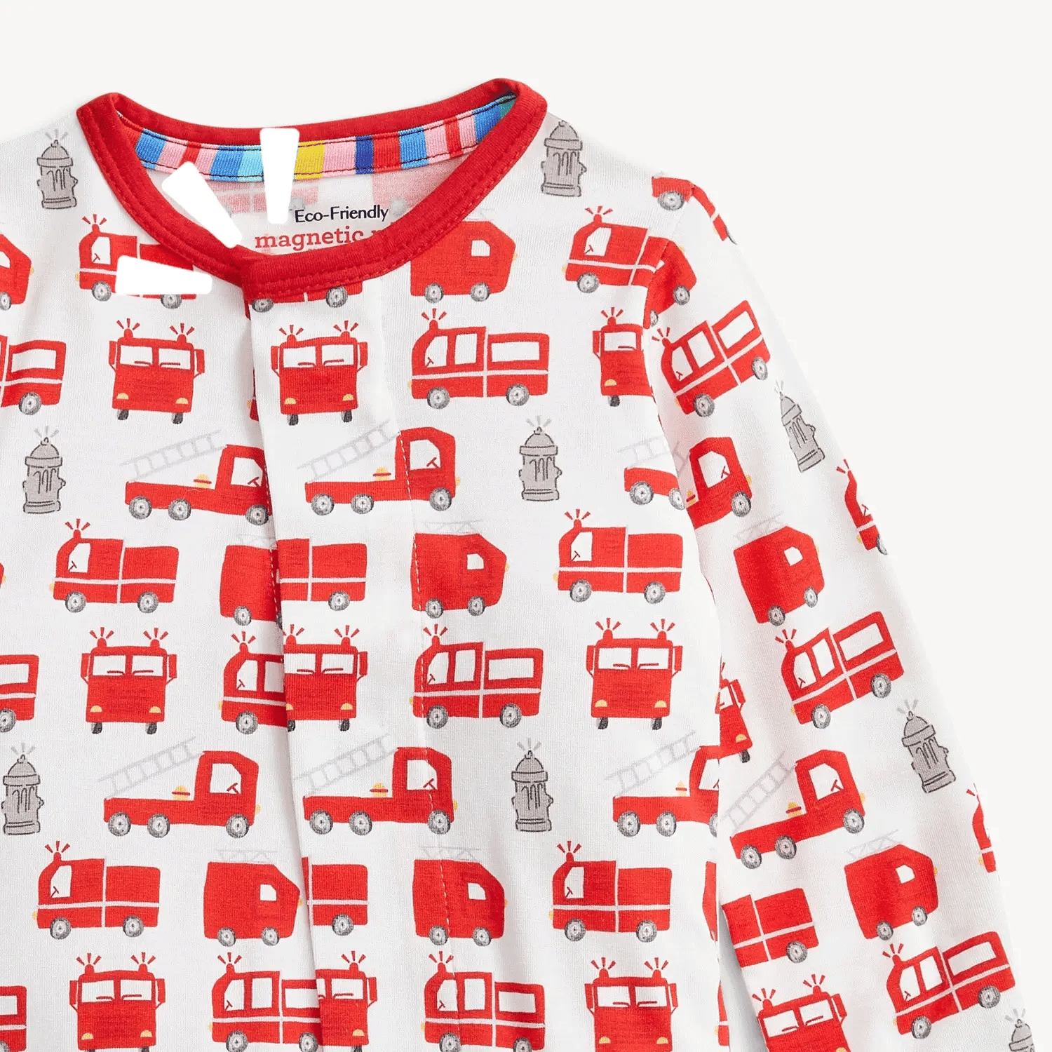 The Magnetic Me "Fired Up" Footie by Magnetic Me is a red and white baby modal sleeper featuring a playful pattern of fire trucks, ladders, and fire hydrants. The collar is trimmed in red with a striped detail on the inner neckline. This long-sleeved footie is made from eco-friendly materials and includes convenient magnetic closures for easy changes.