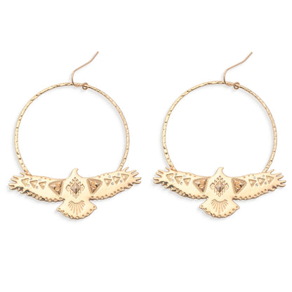 Leslie Curtis Montana Earrings by Leslie Curtis: Gold hammered hoop earrings adorned with intricately detailed, eagle-shaped pendants featuring outstretched wings and etched patterns, showcased against a white background. Ideal for those searching for standout eagle earrings with unique craftsmanship—handle with care to preserve their lasting beauty.