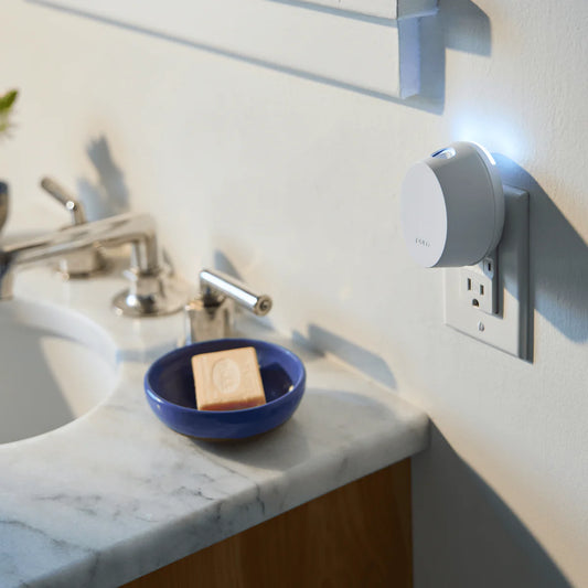 Pura Mini Smart Fragrance Diffuser plugged into outlet above bathroom sink with blue ceramic dish below