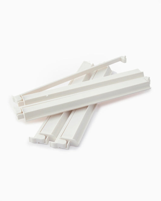Four white rack and pusher sets from the Oh My Mahjong White Rack & Pusher Set by Oh My Mahjong are arranged in a scattered stack on a white background, resembling miniature American mahjong racks or acrylic pushers typically used in mahjong games.