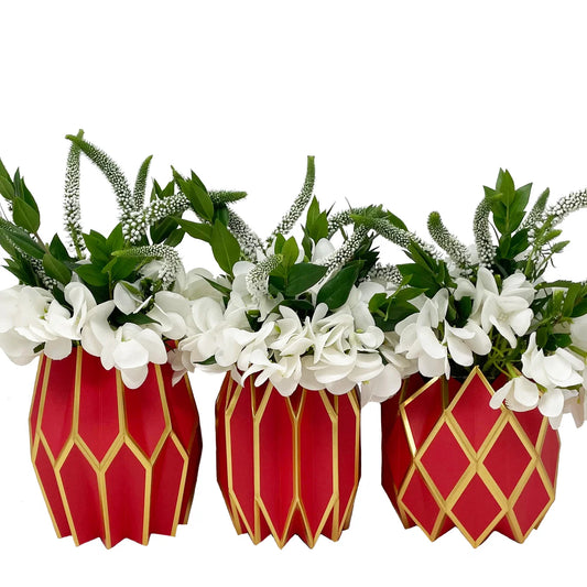 Three Vase Wraps by Lucy Grymes (red & gold) from Lucy Grymes hold arrangements of white flowers and green leaves, displayed against a white background.