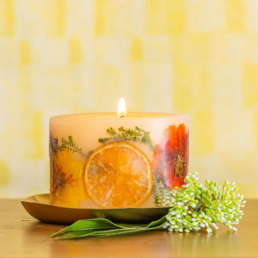 Rosy Rings Petite Botanical Candle lit with orange slices and pressed flowers, accompanied by greenery