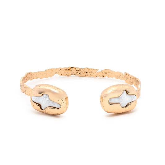 Introducing the Leslie Curtis Spencer Bracelet by Leslie Curtis—a textured gold hammered cuff bracelet with two oval-shaped ends, each featuring a white stone inlaid with delicate white cross accents.