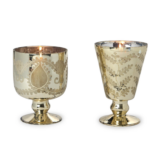 A pair of Two’s Company Etched Mercury Glass Candleholders by Two’s Company, each featuring a lit candle. These vintage-inspired holders showcase intricate etched designs, a reflective mercury glass finish, and rest elegantly on small pedestal bases.
