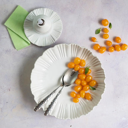 White plate with silver fork and spoon, yellow grape tomatoes on the plate and table, a white condiment bottle, small plate, and green napkin all rest on a light surface—an inviting setting to highlight your Vietri Bari White Shallow Serving Bowl by Vietri. This microwave-safe serving bowl is also dishwasher safe for easy cleanup.