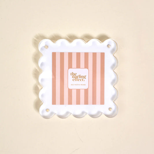 The Darling Effect Square Scalloped Acrylic Frame in white with wavy scalloped edges and brass corner hardware