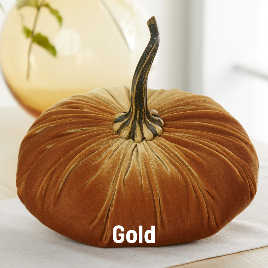 A Your Heart’s Content Pumpkin Extra Large Velvet pillow by Your Heart’s Content, featuring a luxurious gold velvet texture and a realistic stem, sits on a table, serving as an elegant choice for Thanksgiving table decor. The word “Gold” appears overlaid at the bottom center of the image.
