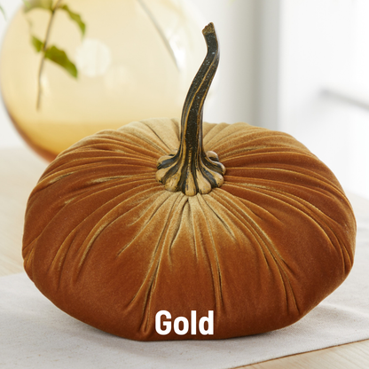 A Your Heart’s Content Pumpkin Extra Large Velvet pillow by Your Heart’s Content, featuring a luxurious gold velvet texture and a realistic stem, sits on a table, serving as an elegant choice for Thanksgiving table decor. The word “Gold” appears overlaid at the bottom center of the image.