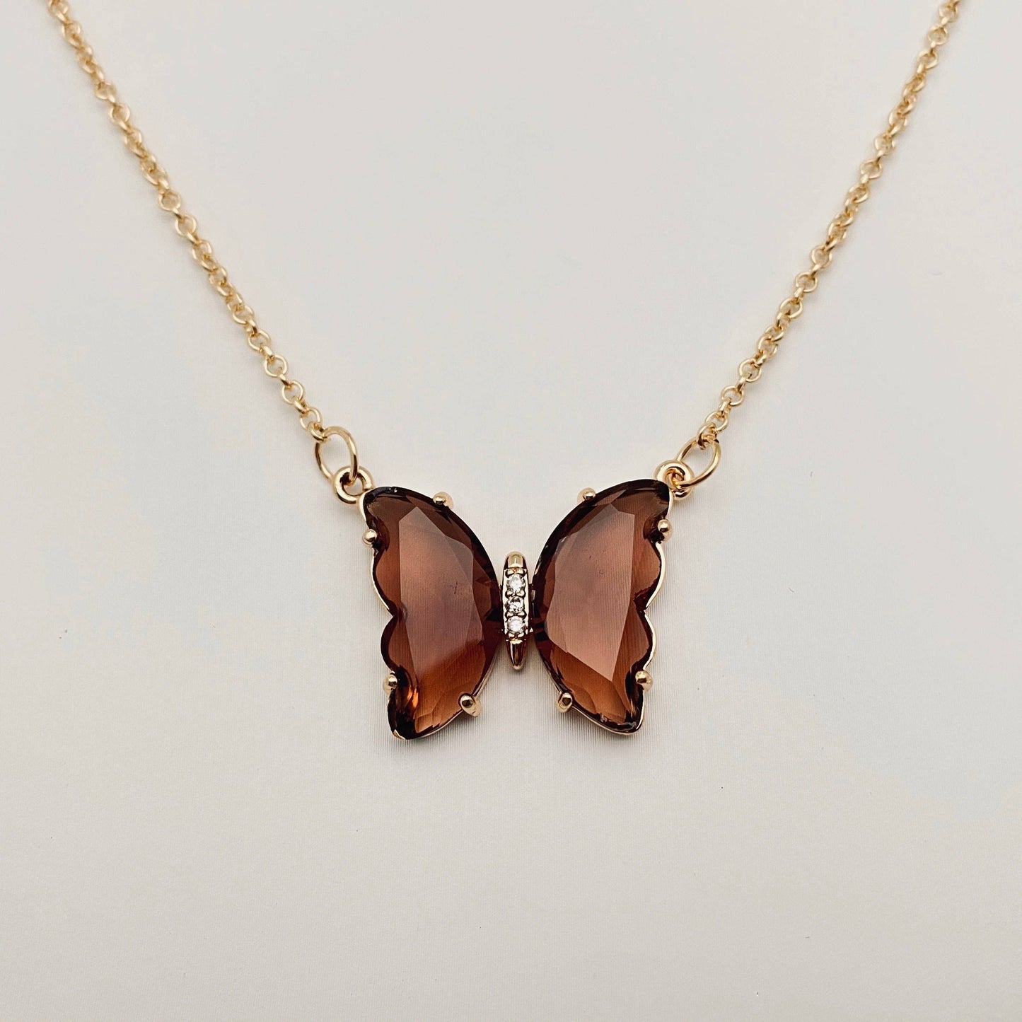 Mio Queena - Multicolor Glass Butterfly Pendant Necklace by Mio Queena, showcased on a plain, light background and designed as hypoallergenic jewelry, features a shimmering glass pendant with multicolor faceted wings resembling gemstones and a delicate row of clear stones in the center.
