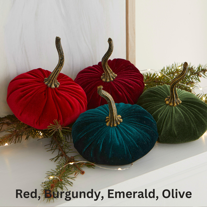 Four “Your Heart’s Content - Pumpkin Small Velvet” pumpkins in red, burgundy, emerald, and olive from Your Heart’s Content are arranged on pine branches with string lights against a white background, creating a stunning Thanksgiving centerpiece that also serves as elegant holiday mantel décor.