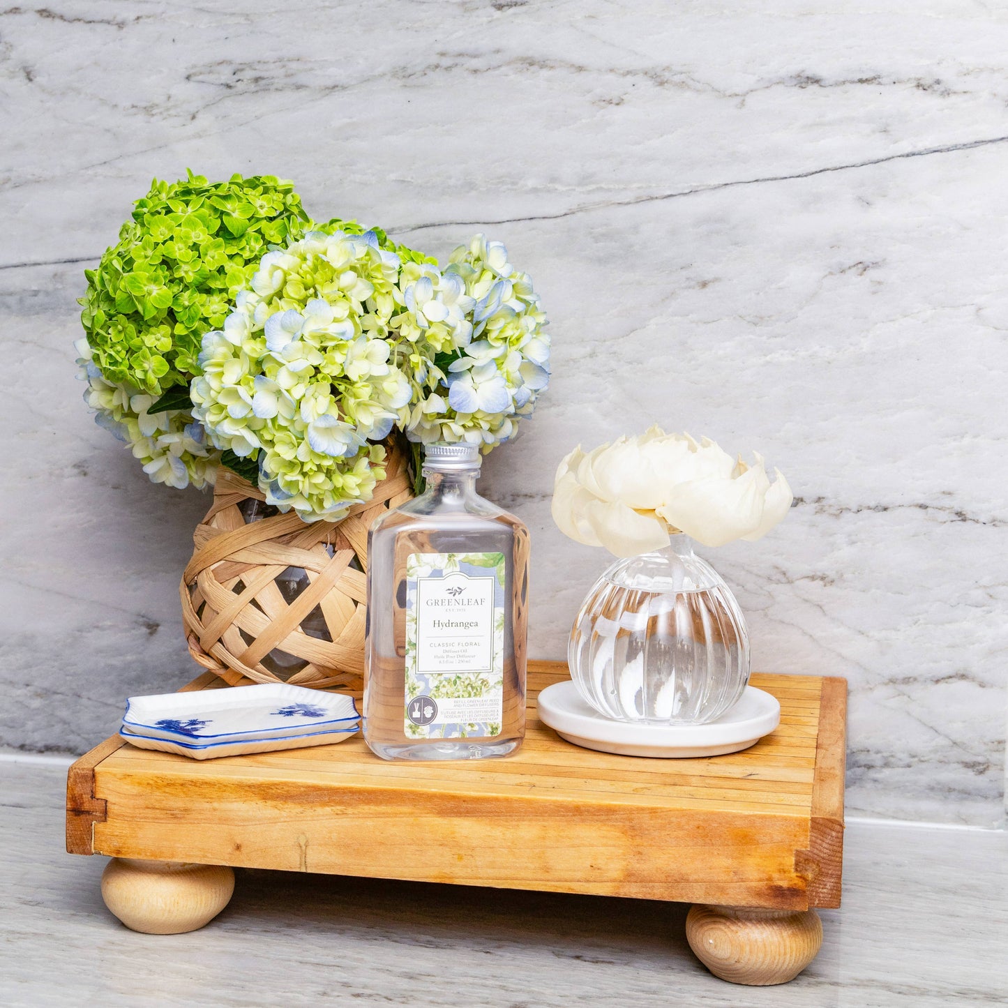 Greenleaf Gifts Hydrangea diffuser bottle displayed on wooden tray with fresh green and white hydrangea arrangement