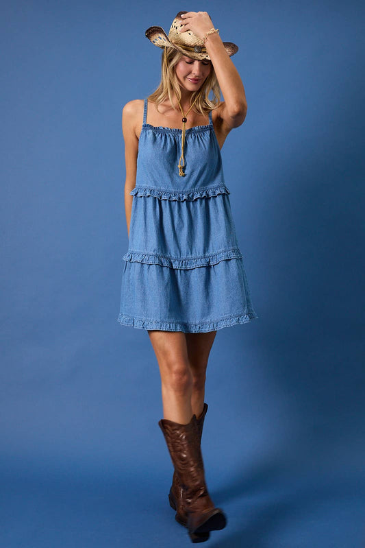 Sunday Edition by LE LIS sleeveless light blue denim mini dress with tiered ruffle detail, worn with brown boots and straw hat