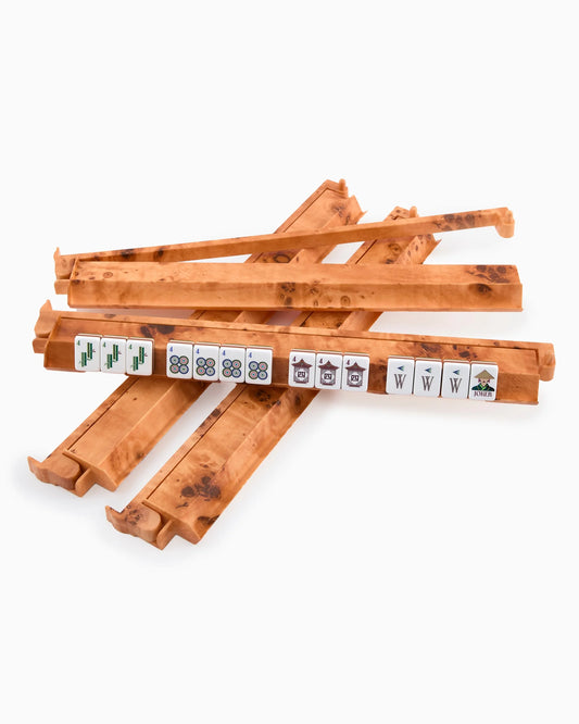Four wooden mahjong racks from the Oh My Mahjong Burl Rack & Pusher Set, featuring mahjong tiles arranged to display various suits and symbols, are shown alongside a sleek Oh My Mahjong Burl Rack, all set against a plain white background.
