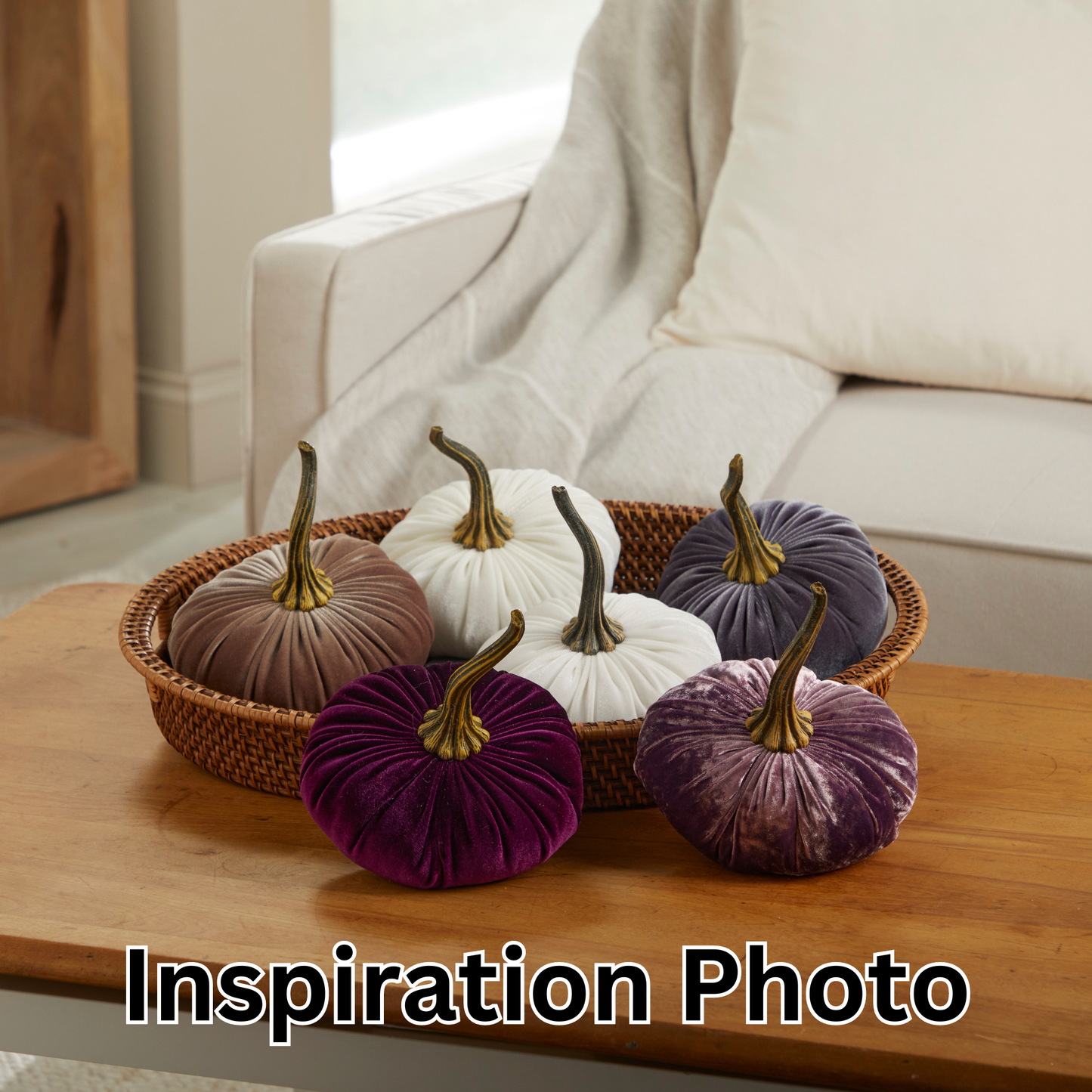 A woven basket filled with six “Your Heart’s Content - Pumpkin Large Velvet” pumpkins in elegant shades of white, brown, and purple from Your Heart’s Content sits on a wooden coffee table in front of a white sofa, creating an inviting Thanksgiving centerpiece or charming holiday mantel decor.