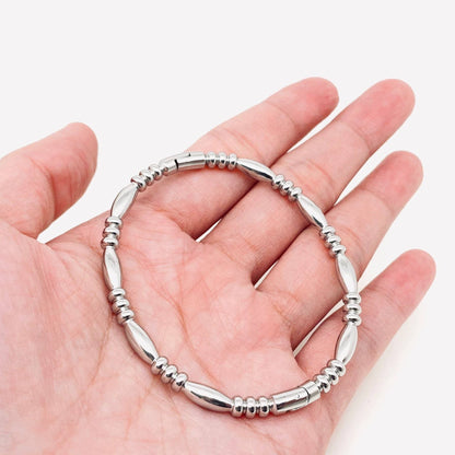 A hand holding the Mio Queena Multi-style 18K Gold-plated Stainless Steel Bangle, featuring alternating oval and round bead shapes with a striking gold finish, against a white background—an ideal jewelry gift for any occasion from Mio Queena.