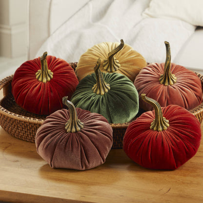 Six large velvet pumpkins from Your Heart’s Content, in assorted fall colors like red, green, gold, orange, and brown, are beautifully arranged in a woven basket on a wooden table with a white sofa in the background—creating an eye-catching handcrafted decor piece with Your Heart’s Content Pumpkin Large Velvet that’s perfect as a Thanksgiving or Halloween centerpiece.