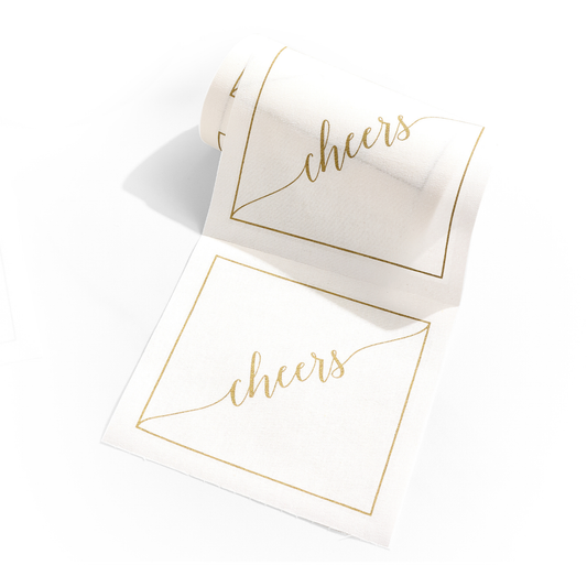 Table Theory Golden Salute cocktail napkins with gold 'cheers' text and border