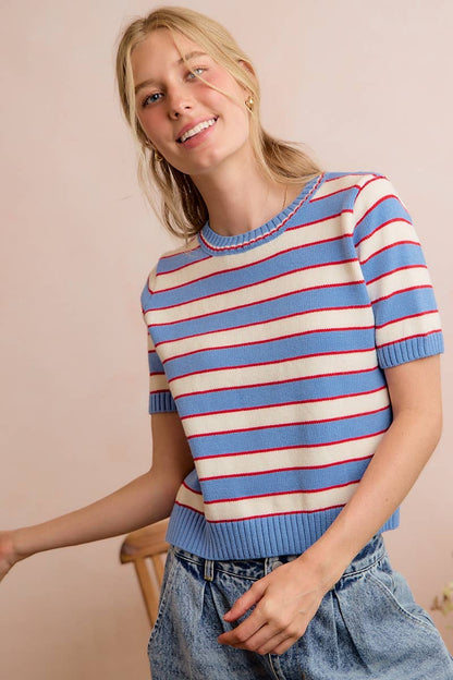 Wearing the So Me - STRIPE KNIT CREW NECK SHORT SLEEVES SWEATER TOP by So Me, paired with light blue jeans, a person stands smiling against a pale pink background.