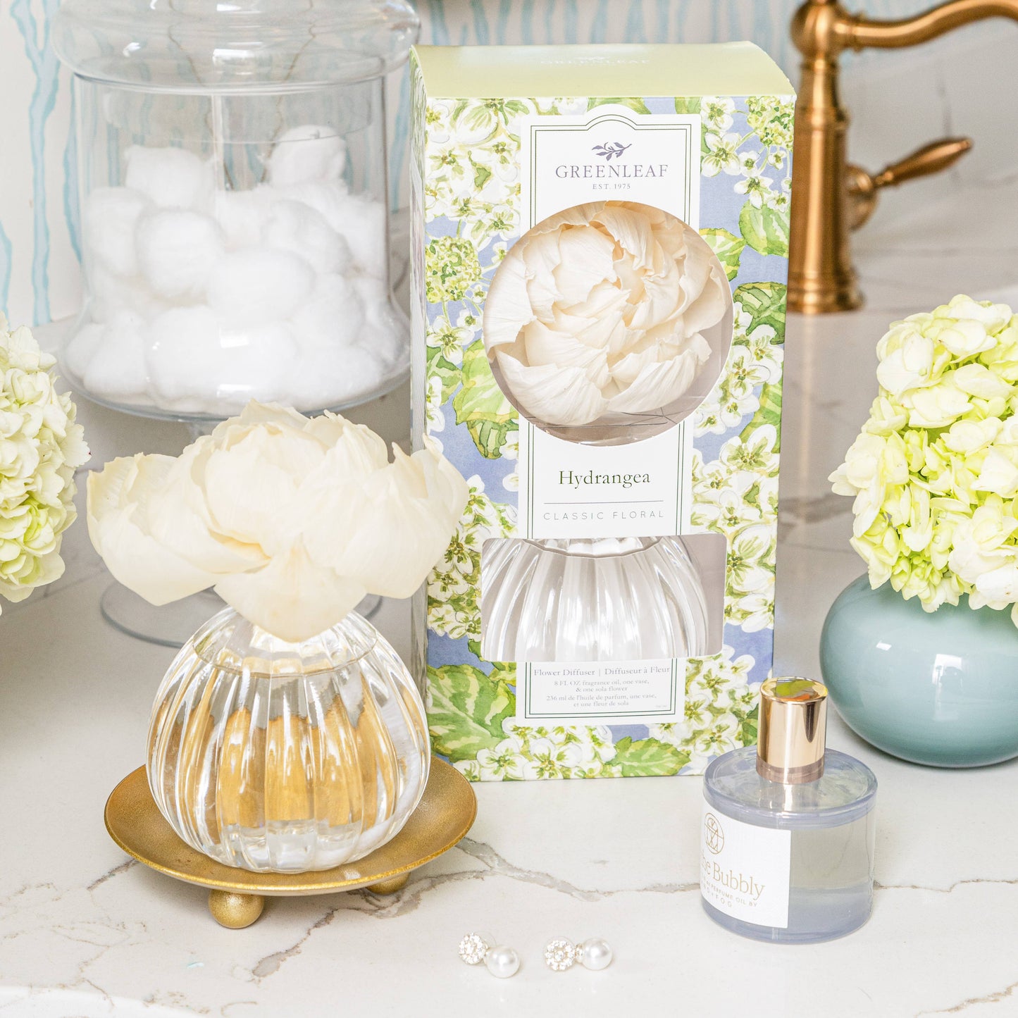 Greenleaf Gifts Hydrangea diffuser with cream flower on ribbed glass base styled on marble bathroom counter with fresh hydrangeas