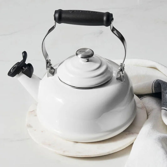 Le Creuset Classic Whistling Kettle in white with black handle and spout, on marble surface