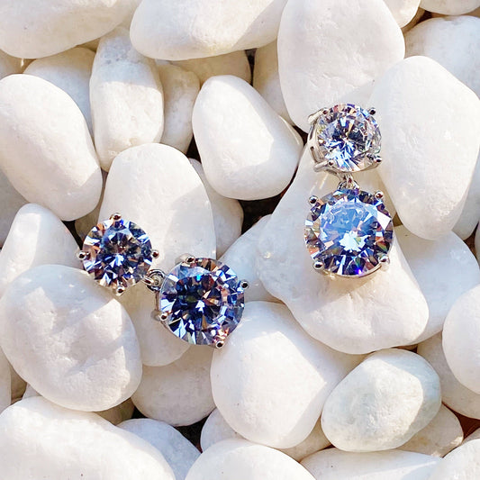 Ellison+Young double diamond dangle earrings on white quartz, featuring paired round brilliant-cut blue and clear stones in silver settings