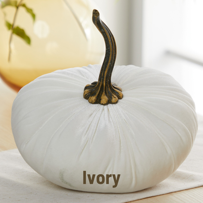 An extra large ivory velvet pumpkin from Your Heart’s Content, featuring a dark, curved stem, sits atop a table and adds a charming touch to wedding centerpiece arrangements. The phrase “Ivory” appears below in bold lettering, while a yellow vase with green leaves is softly blurred in the background.