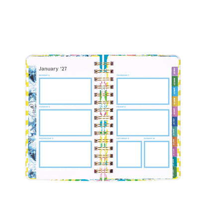 An open spiral-bound planner, the Lilly Pulitzer by Lifeguard Press - Medium 17 Month Agenda in Lovely Lilly, displays a vibrant weekly layout for January 4–10, 2027. Colorful borders frame each page, with a blank blue box for notes on each day and cheerful tabs along the right edge labeling the days of the week.