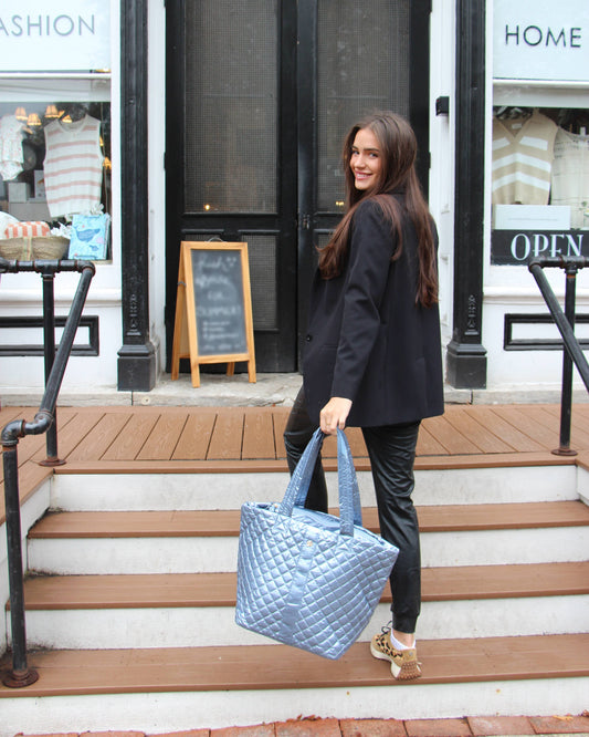 Woman wearing black blazer carrying ice blue quilted diamond tote bag on storefront steps