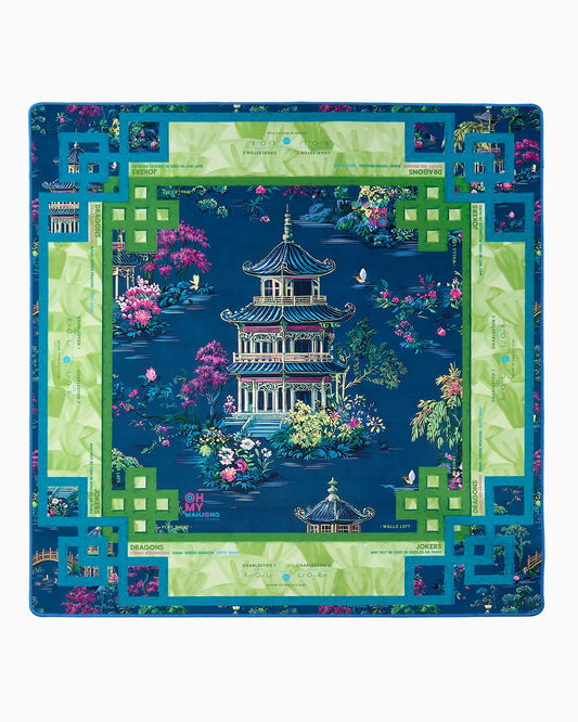 Introducing the Oh My Mahjong Elysium Mat in Tube by Oh My Mahjong—a square mat adorned with a blue and green border, showcasing an intricate Asian-inspired pagoda design surrounded by pink flowers, lush greenery, butterflies, and decorative text details; a vibrant and ornate piece reminiscent of a decorative gaming mat.