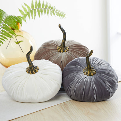 Three extra large velvet pumpkins from Your Heart’s Content in white, brown, and gray rest on a light table, creating an elegant wedding centerpiece or charming Thanksgiving table decor. Each pumpkin from Your Heart’s Content features a signature gold and black stem, while in the background, a yellow vase with a green fern adds a fresh touch.