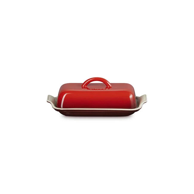 Le Creuset Heritage Butter Dish by Le Creuset, shown in red with a rectangular ceramic design, side handles, and a matching red lid with a centered handle on a white background.