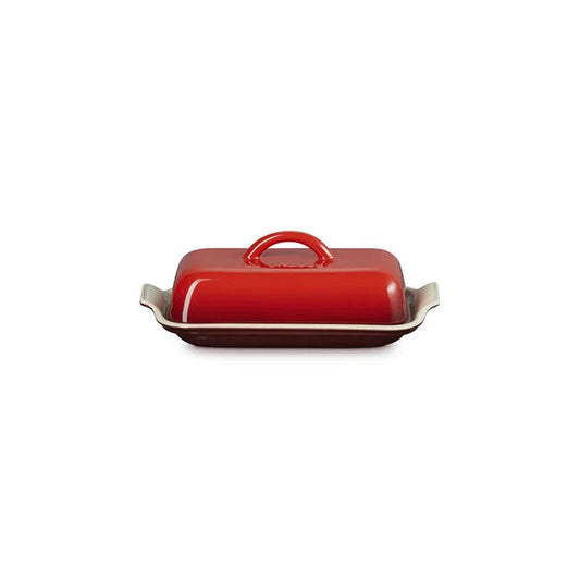 Le Creuset Heritage Butter Dish by Le Creuset, shown in red with a rectangular ceramic design, side handles, and a matching red lid with a centered handle on a white background.