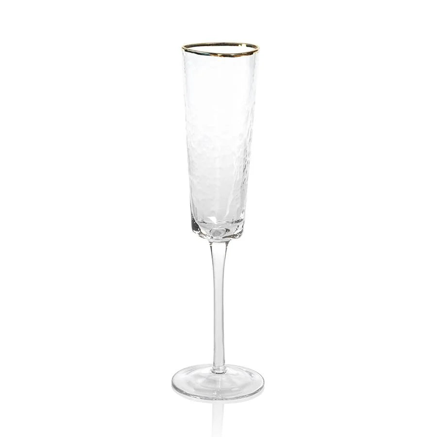 The Zodax "Kampari" champagne flute is a clear, textured glass with a long stem and a delicate gold rim, shown standing upright on a white background.