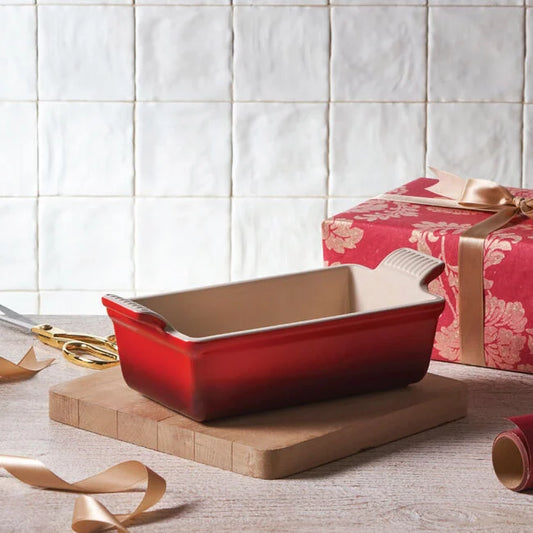 Le Creuset Heritage red loaf pan on wooden trivet with gift wrap styling