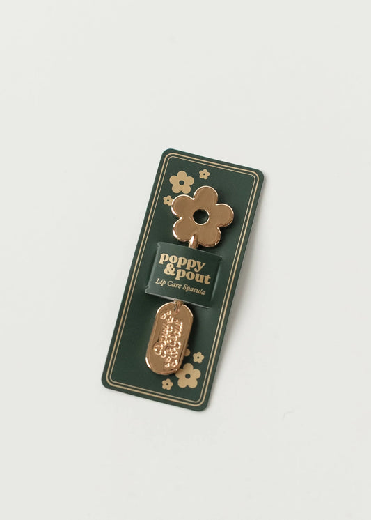 Poppy & Pout Lip Care Spatula in gold with flower design on forest green packaging