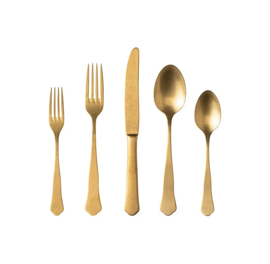 Five gold-colored Costa Nova "Prado - Gold" stainless steel utensils—a salad fork, dinner fork, knife, soup spoon, and teaspoon—are arranged in a row on a white background.