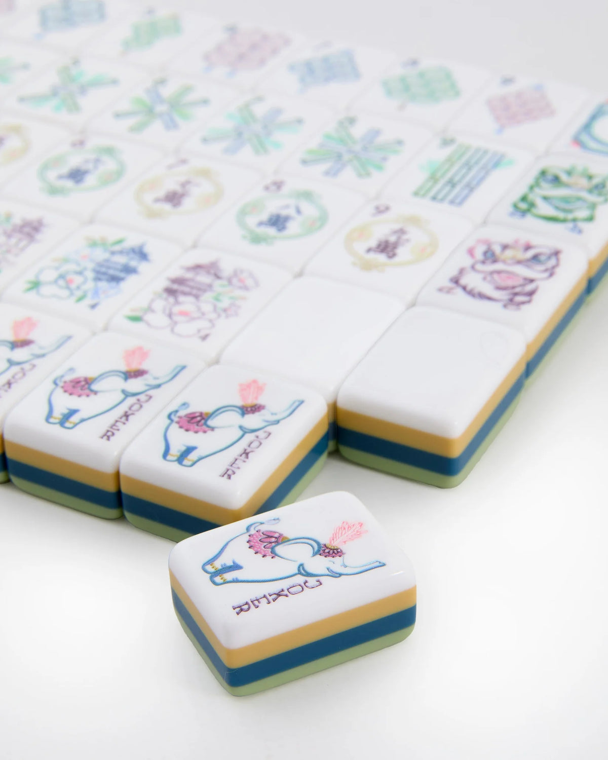 A close-up of the elegant Oh My Mahjong Willow Tiles set by Oh My Mahjong, with most tiles arranged in rows and one tile—adorned with a colorful elephant illustration—placed prominently in the foreground, distinct from the others.