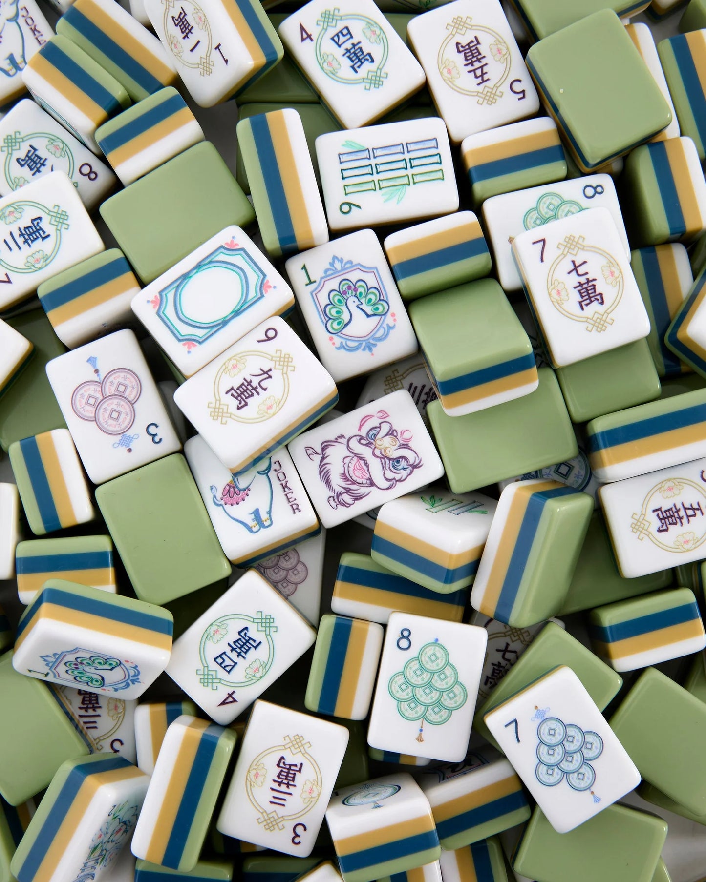 A collection of Oh My Mahjong Willow Tiles by Oh My Mahjong, featuring various symbols and numbers in shades of green, white, and yellow, are scattered and overlapping one another in the image.