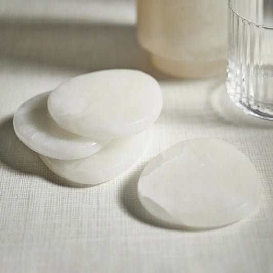 Zodax La Salama alabaster coasters in white stone, oval shaped, arranged on white linen surface